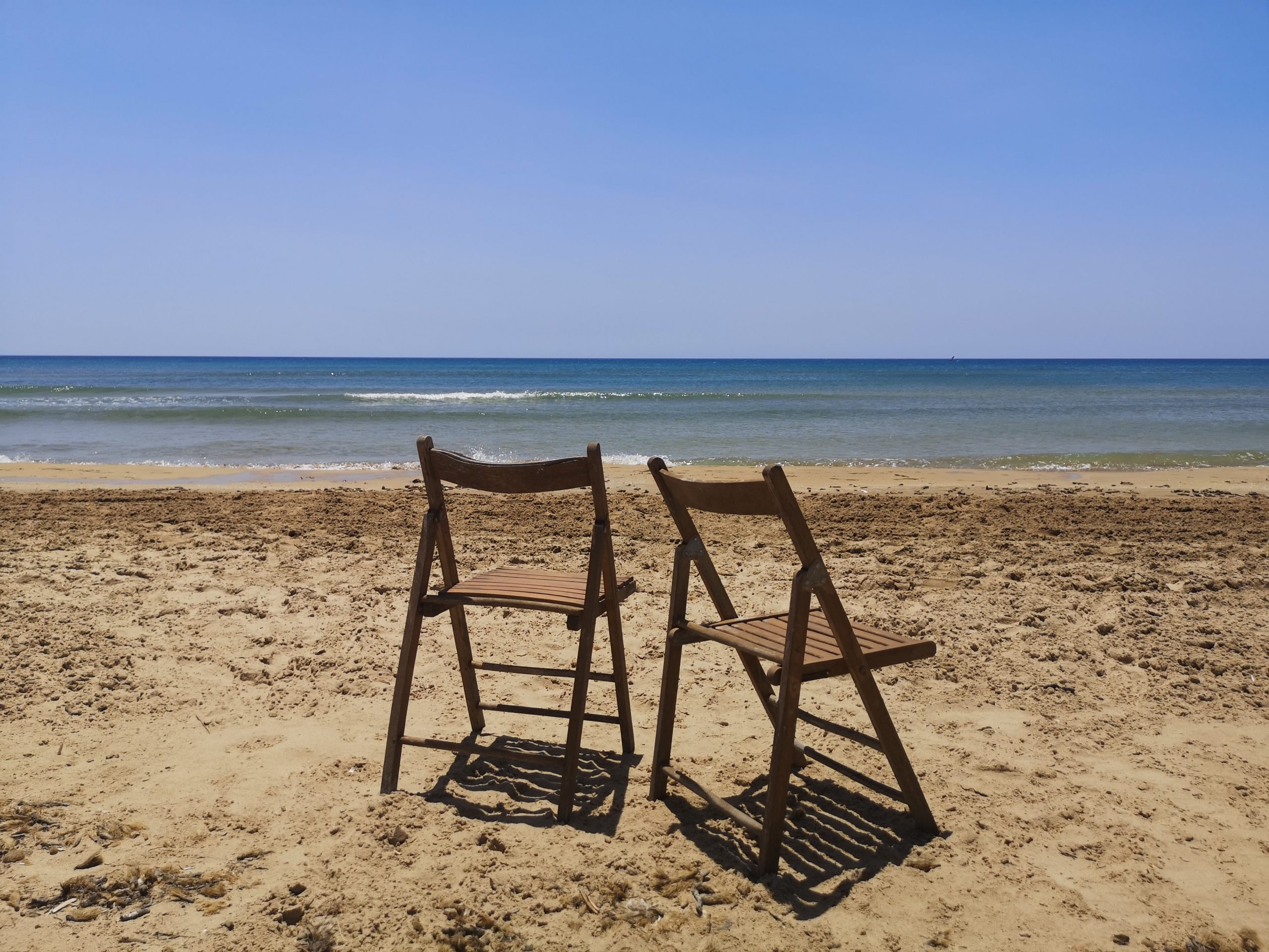 spiaggia con due sedie di legno pieghevoli che guardano il mare